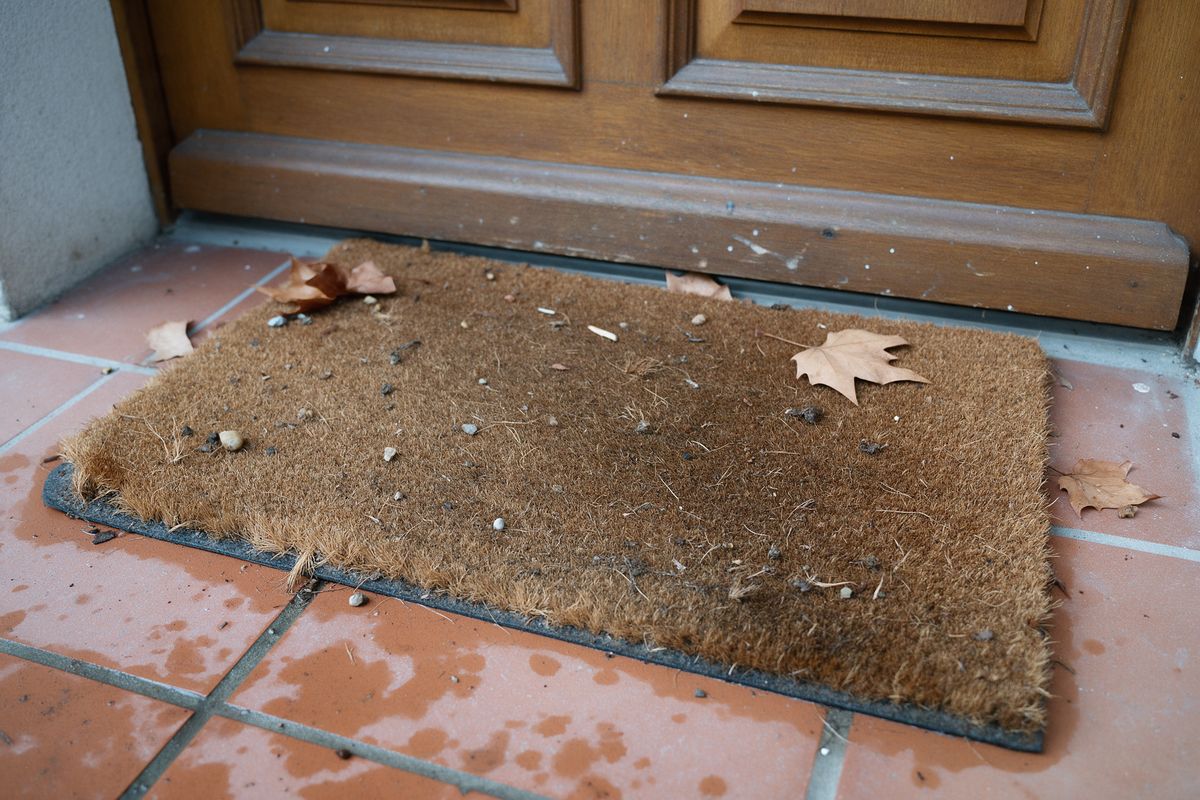 Paillasson coco dont les fibres retiennent gravillons et feuilles mortes devant une entrée